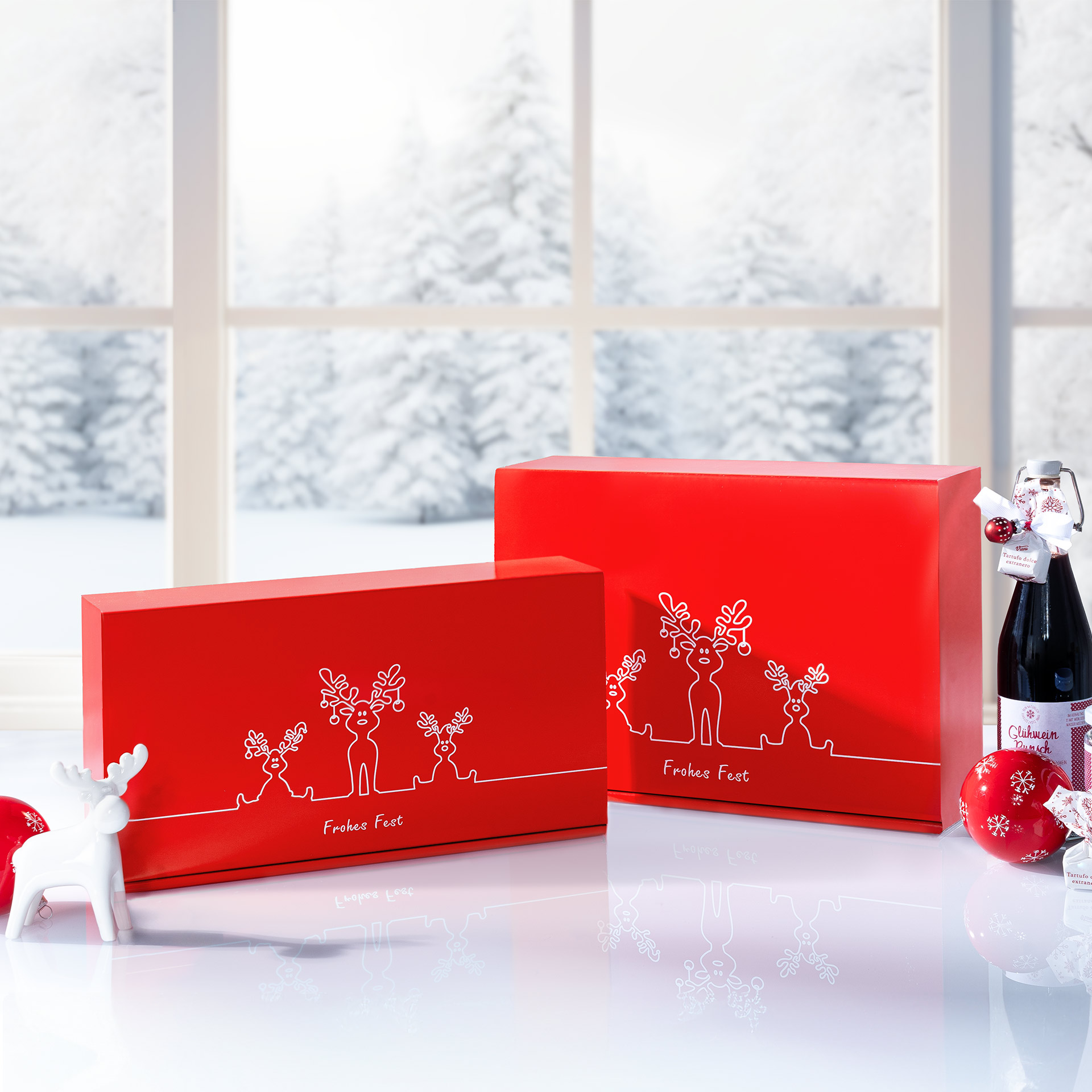 Rote Geschenkboxen mit Rentier Trio Design vor einem winterlichem Fenster.