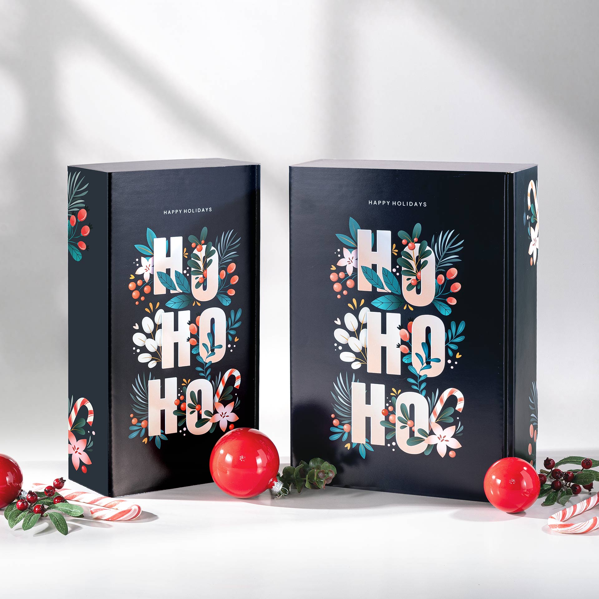 Zwei Geschenkverpackungen mit dem Design Hohoho im Vordergrund mit weihnachtlichen Elementen