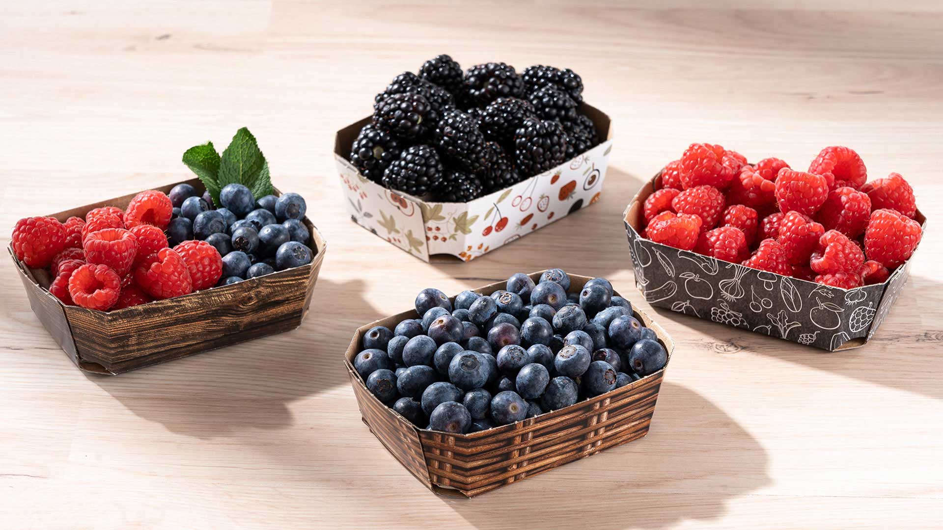 Vier Beerenschalen aus Wellpappe 125g mit verschiedenen Beeren auf einem Tisch